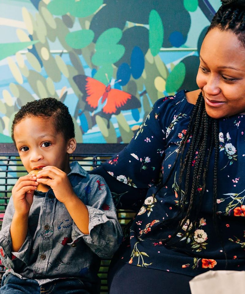 Mother and young son sitting together in front of a colorful mural