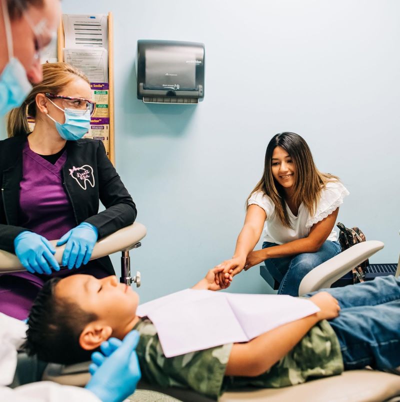 Hygienist treating a young patient while his mother watches at Smile Magic in Zaragoza, El Paso