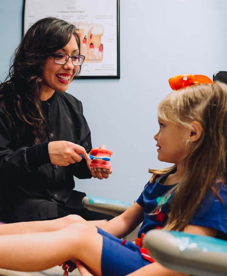 Hygienist showing a young patient a model of her teeth at Smile Magic in Houston