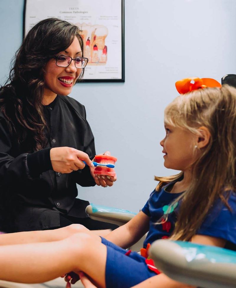 Hygienist showing a young patient a model of her teeth at Smile Magic in Houston
