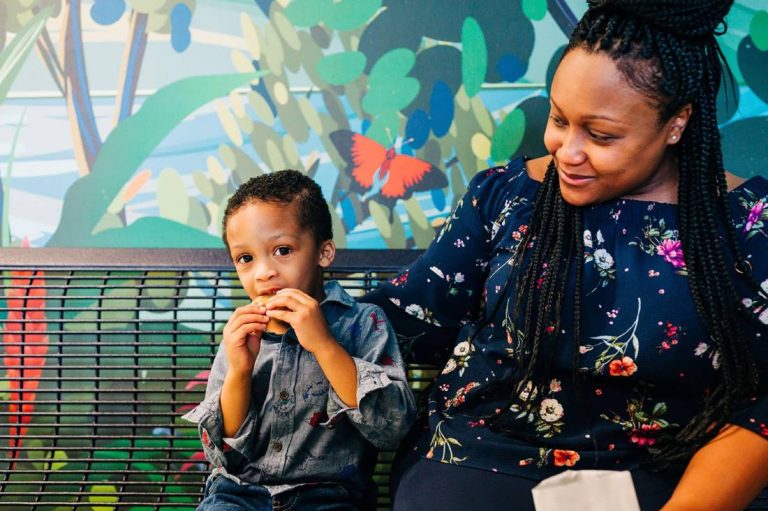 Mother and young son sitting together in front of a colorful mural